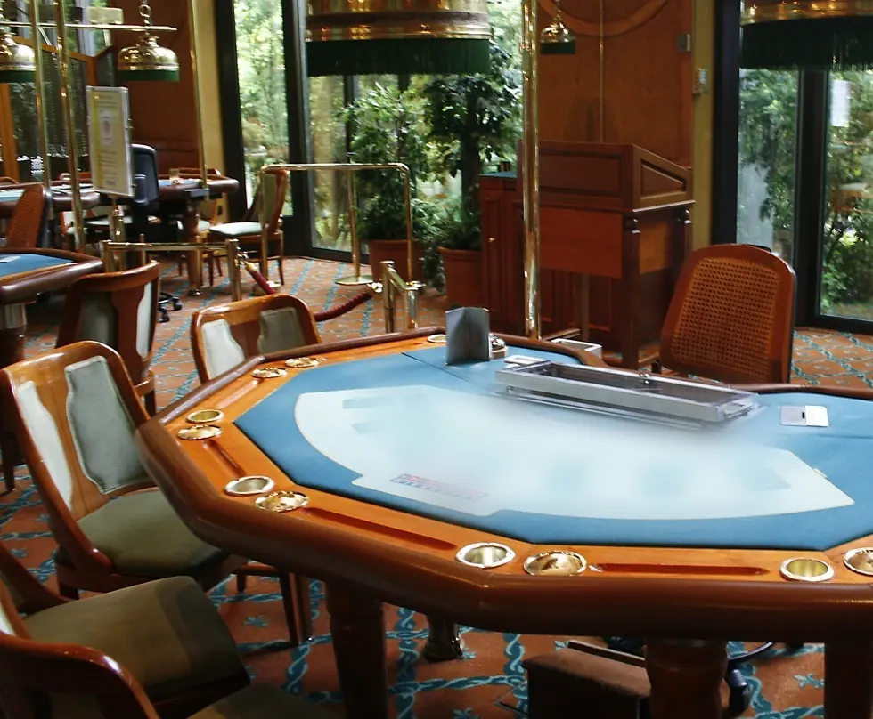 Kék posztós blackjack-asztal fa kávával, beépített pohártartókkal és kárpitozott székekkel egy kaszinóteremben