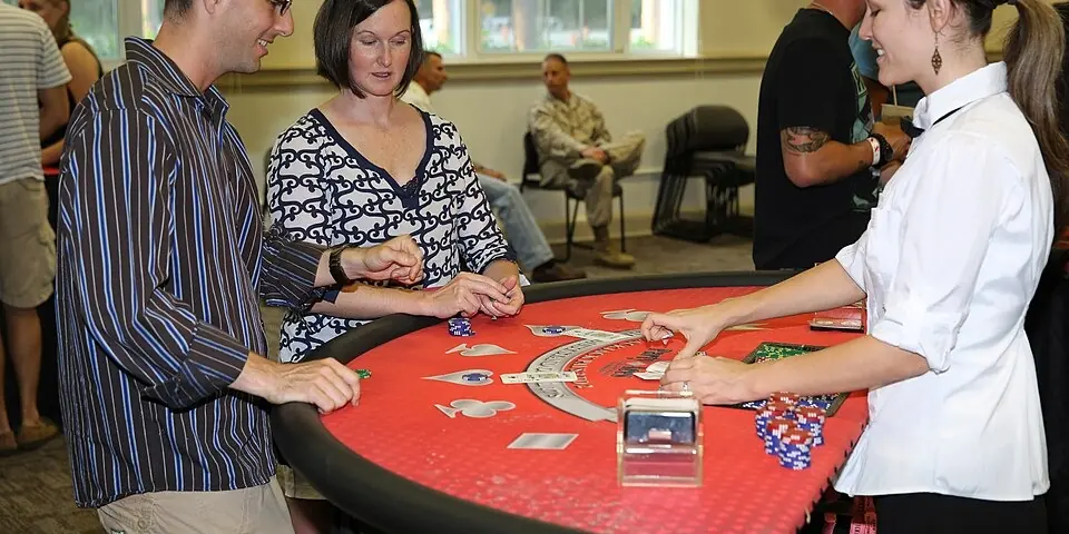 Piros posztós blackjack-asztal egy rendezvényen: az osztó átlátszó kártyaadagoló mellett oszt, két játékos figyel