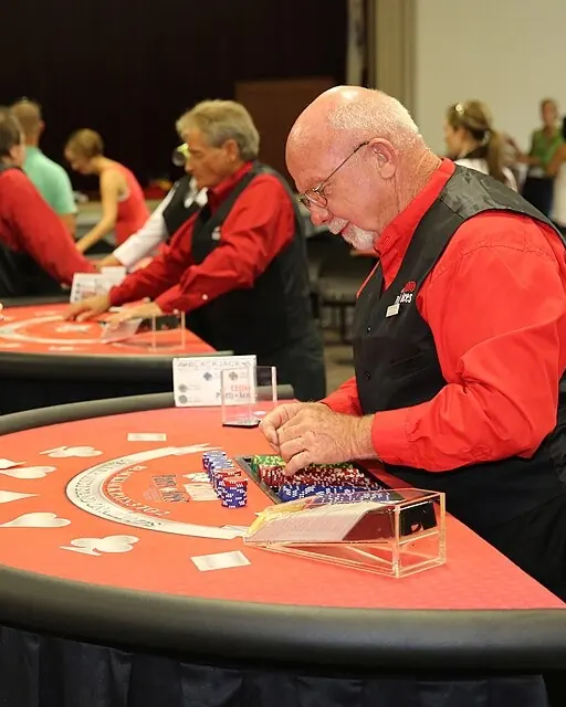Osztó zsetonokat rendez egy piros posztós blackjack-asztalon, előtte átlátszó kártyaadagoló