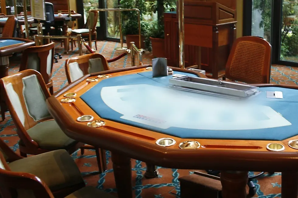 Kék posztós blackjack-asztal fehér nyomott ívvel és felirattal, a fa kávába süllyesztett pohártartókkal