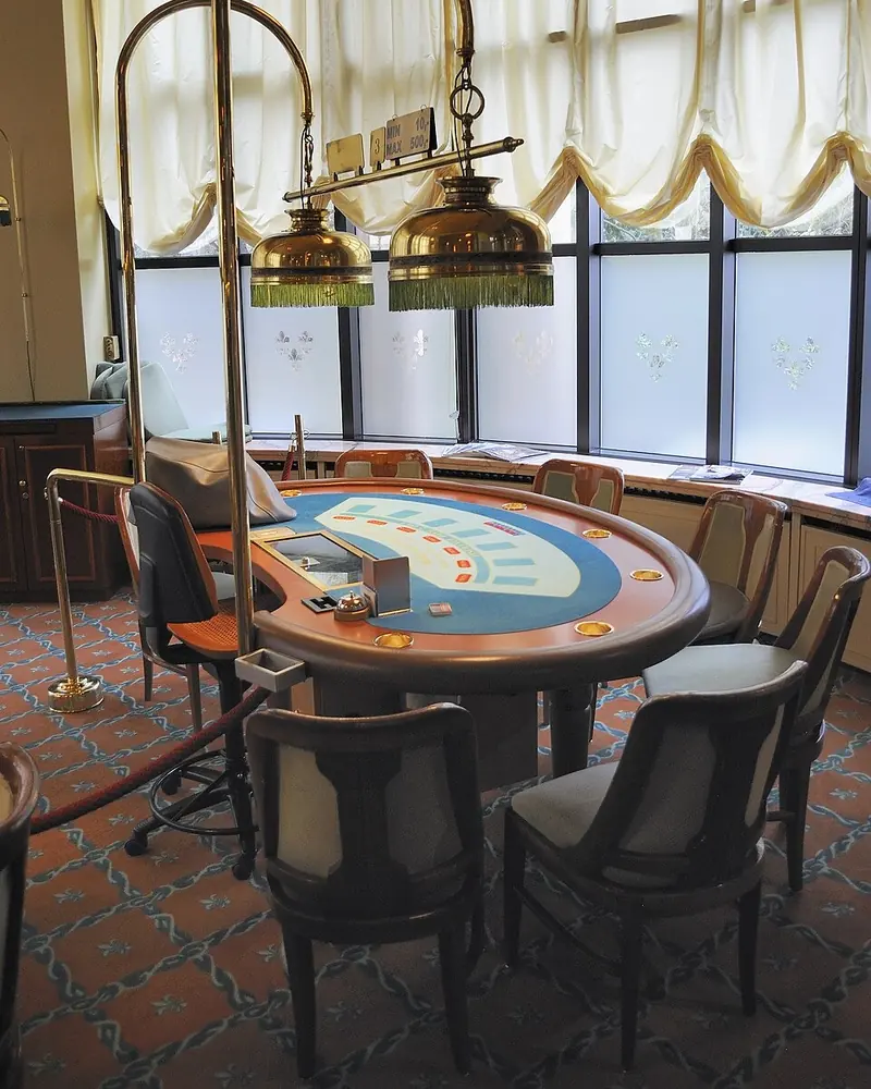 Blackjack-asztal kék posztóval és kárpitozott székekkel két réz függőlámpa alatt egy kaszinóteremben